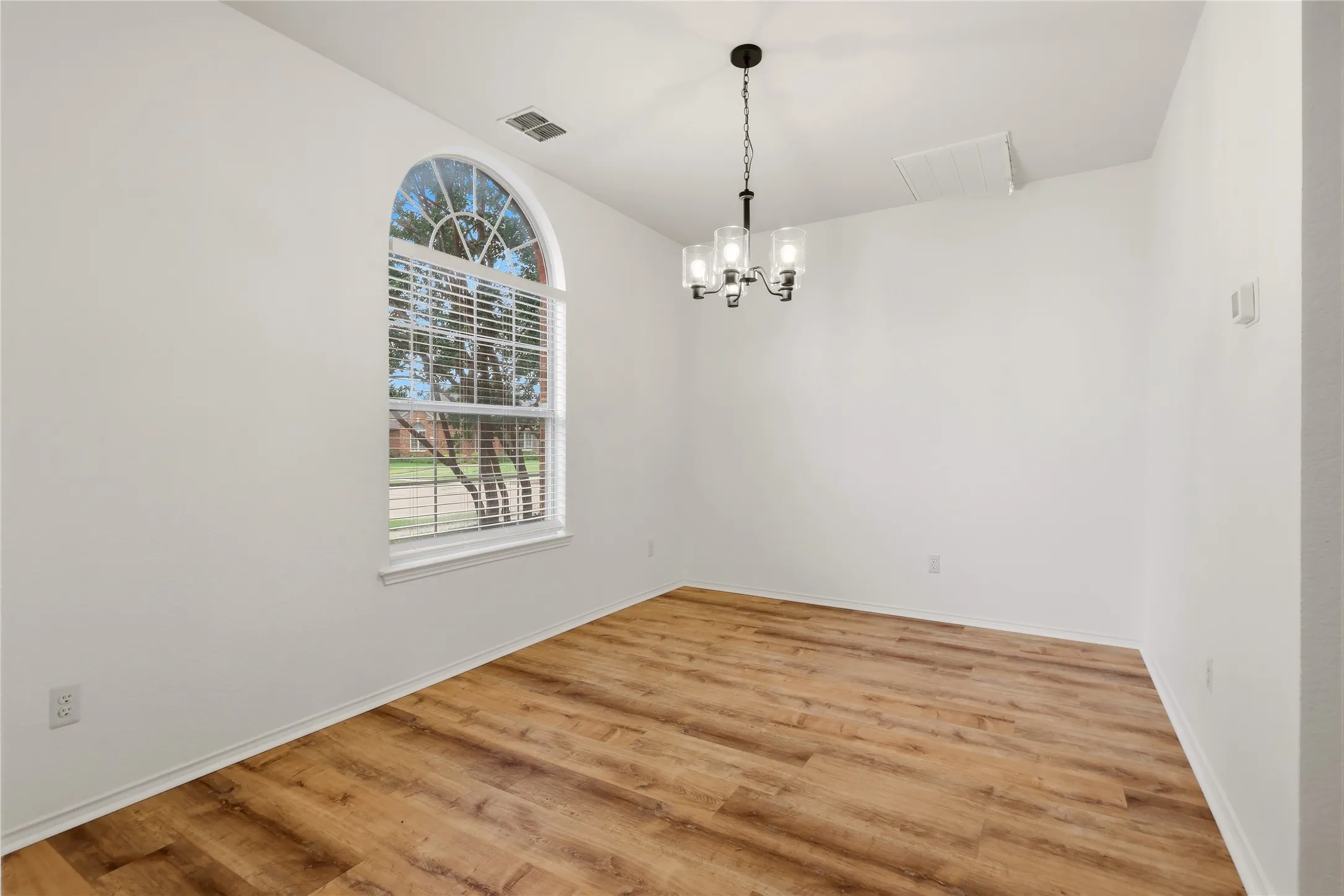 Arched window, wood-finish flooring, ceiling-mounted chandelier, crisp white walls