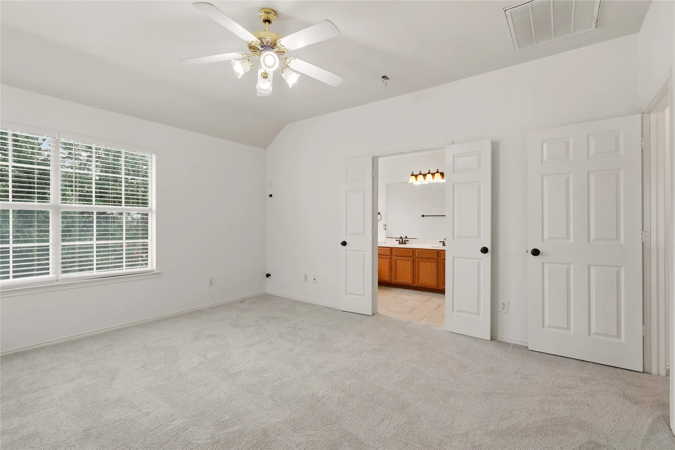 Vaulted ceiling with ceiling fan, large window with blinds, light-toned carpeting, and panel doors