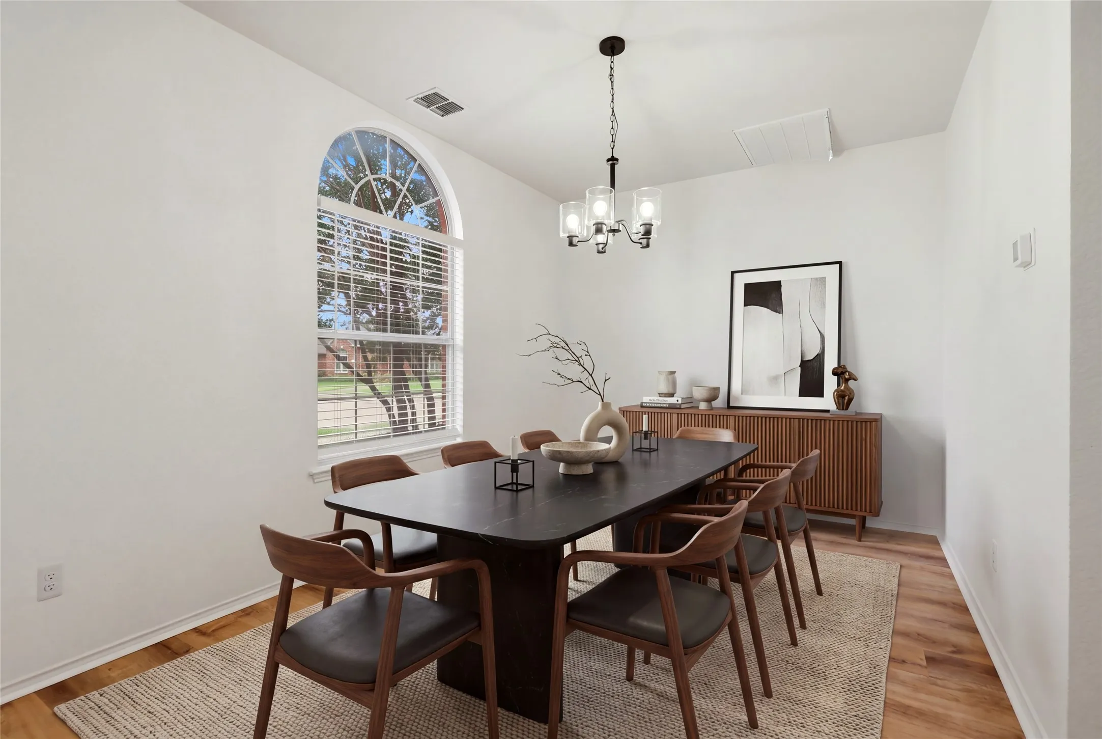 Arched window with blinds, wood-finish flooring, and a contemporary chandelier.  Virtually staged.