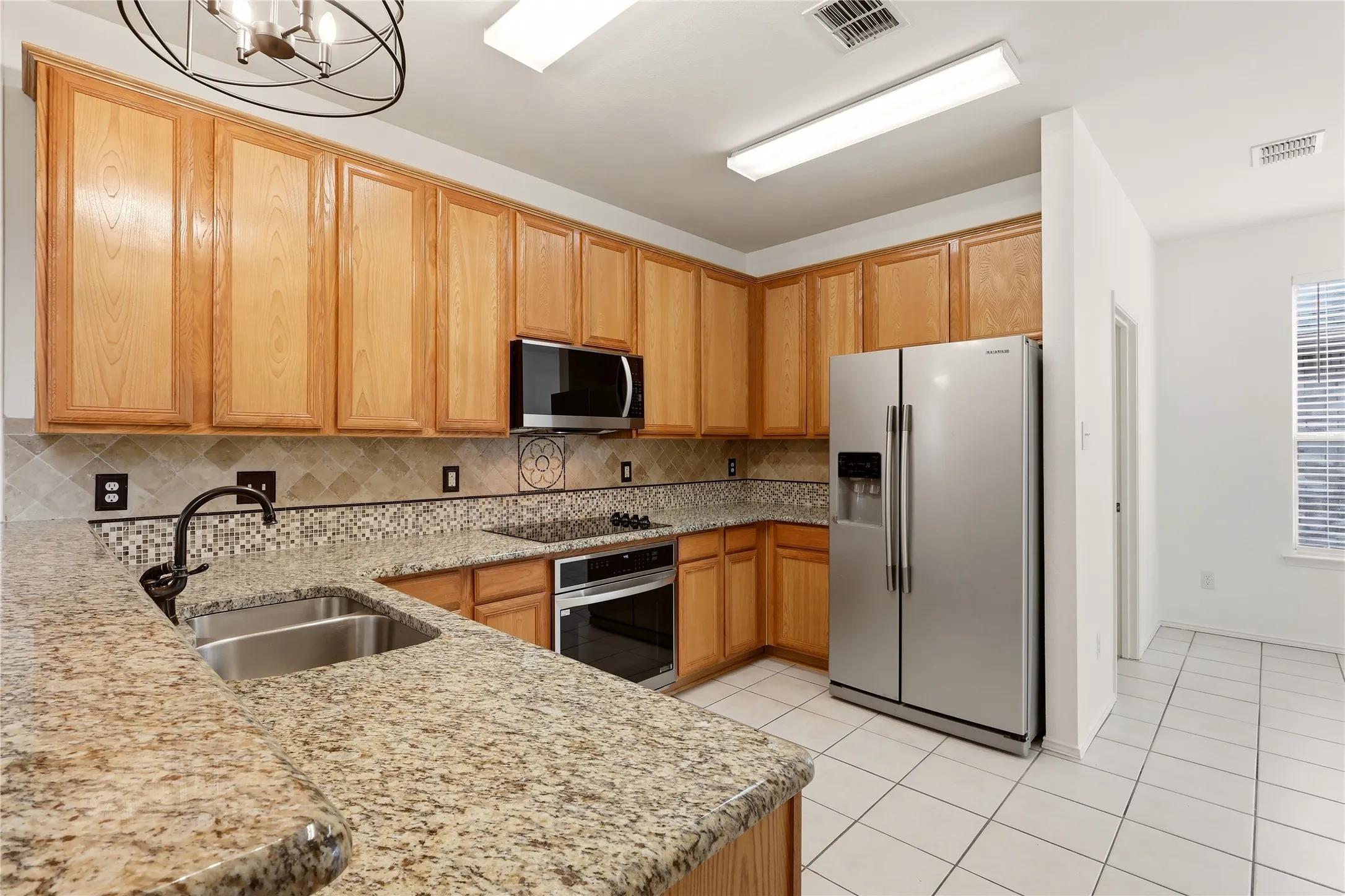 Kitchen featuring granite-style countertops, wood-finish cabinetry, stainless steel appliances, a tile backsplash, and tile flooring