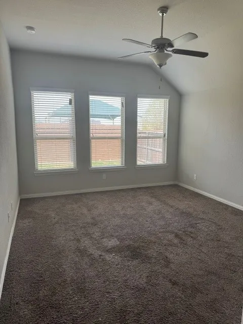 Vaulted ceiling, ceiling fan with integrated lighting, three windows, and carpet flooring