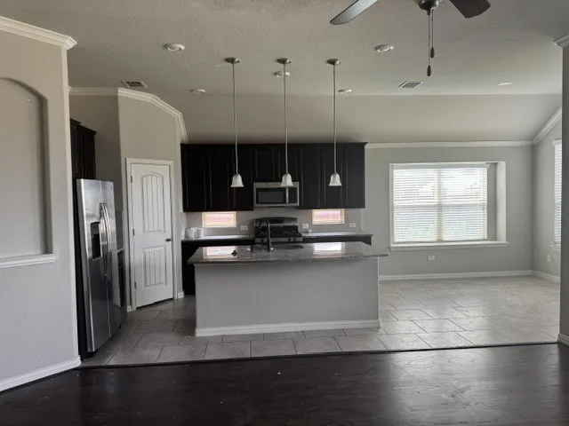Kitchen island with pendant lighting and integrated sink, stainless steel refrigerator, dark wood cabinetry, tile flooring, and wood-finish flooring