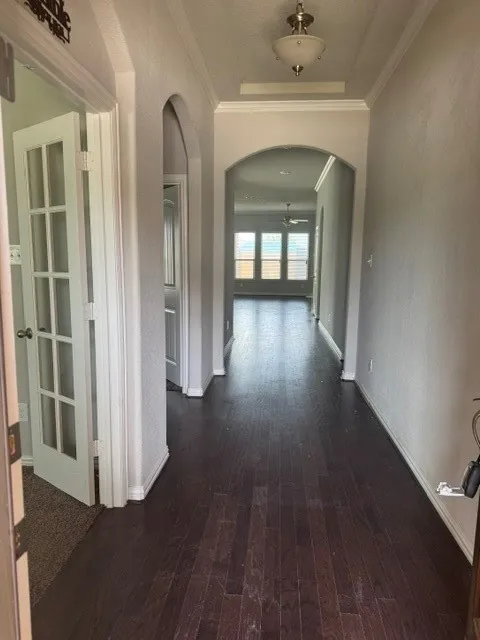 Hallway featuring dark wood-finish flooring, arched doorways, crown molding, and a semi-flush mount light fixture