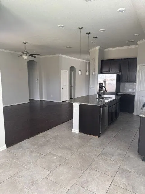 Kitchen island with dark cabinetry, integrated sink, and pendant lighting
