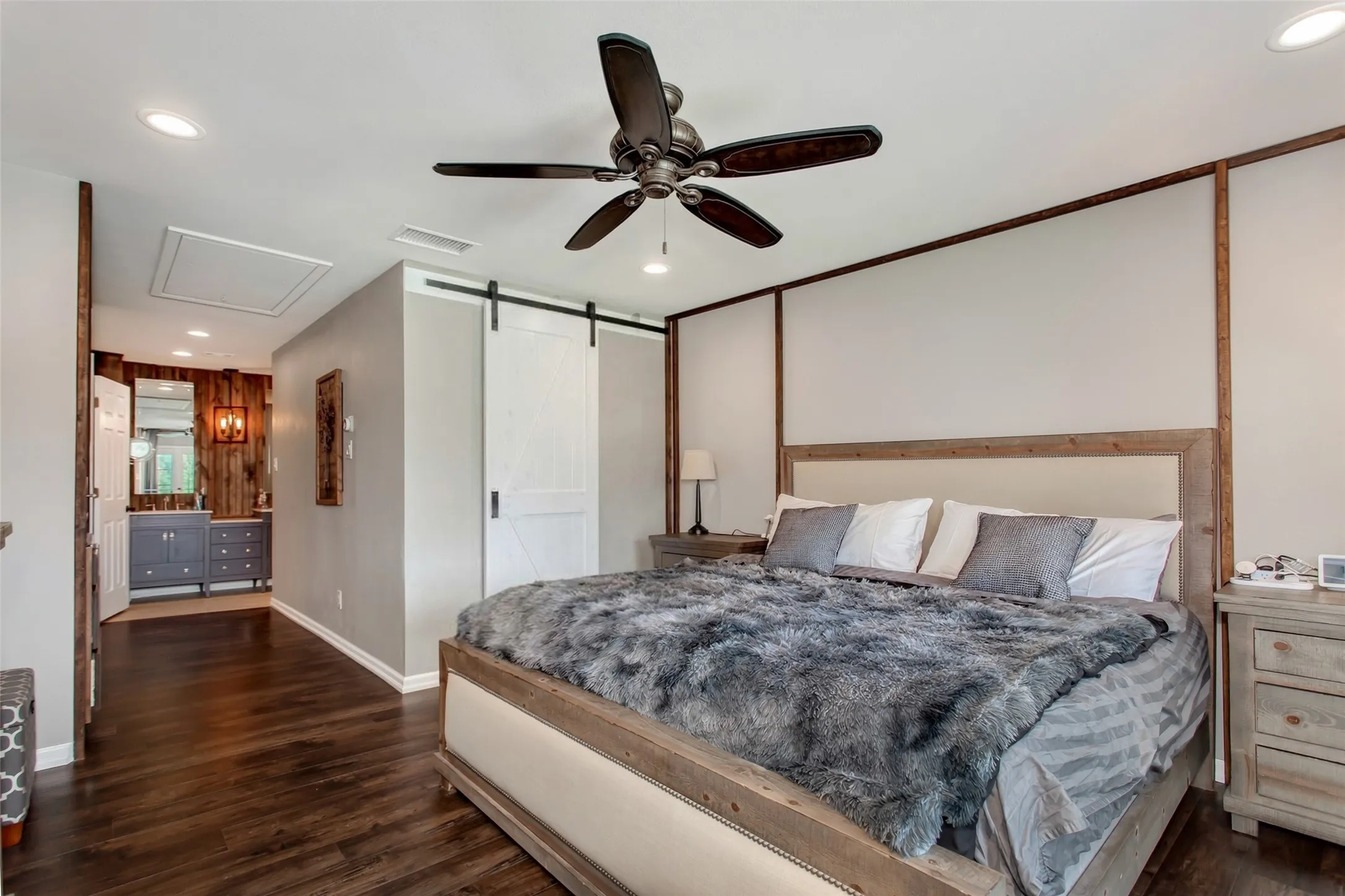 Wood-finish flooring, recessed ceiling lighting, a ceiling fan with integrated lighting, a sliding barn door, and a built-in vanity with dual sinks