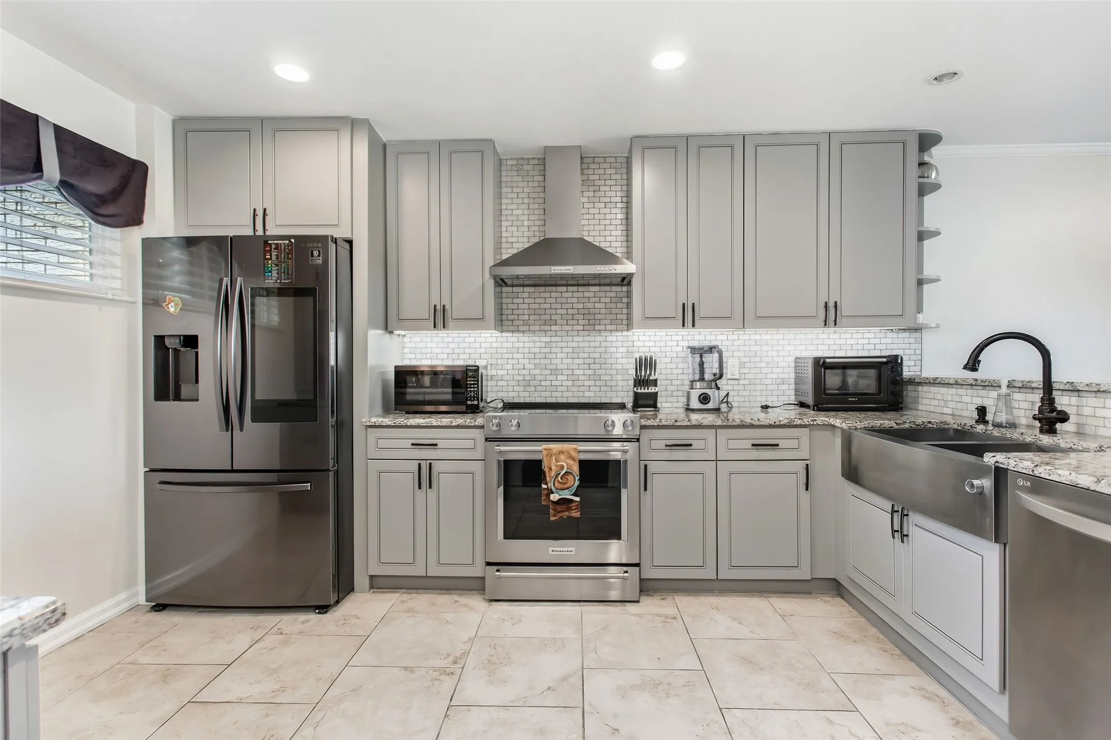 Modern kitchen featuring light gray cabinetry, stainless steel appliances, a subway tile backsplash, granite countertops, and light-toned tile flooring