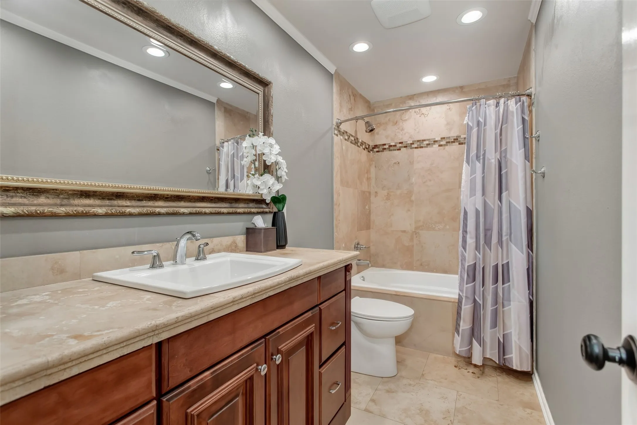 Bathroom featuring a wood-finish vanity with an undermount sink, a light-toned countertop, and a tiled shower-tub combination with a decorative accent band