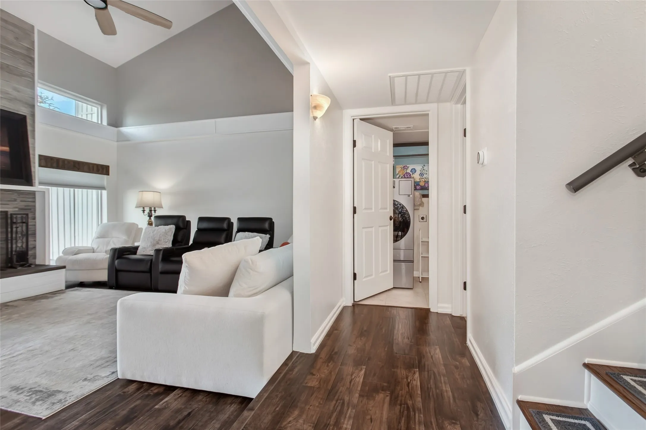 Vaulted ceiling with a ceiling fan, fireplace with a stone surround, wood-finish flooring, and a dedicated laundry area