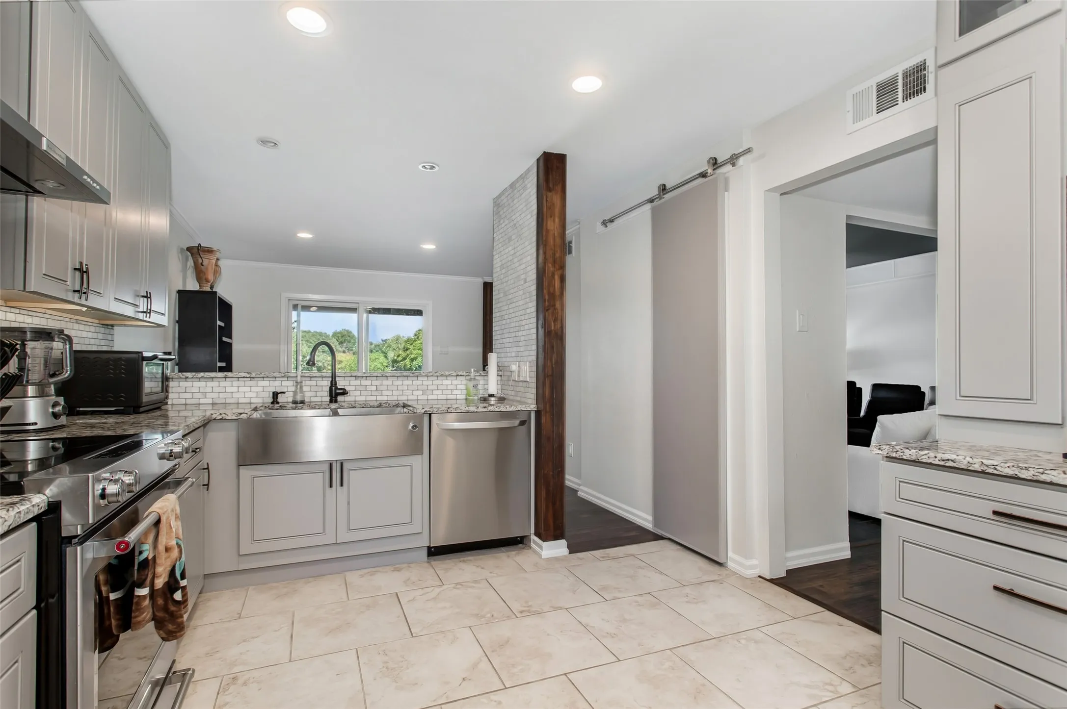 Kitchen featuring light-toned cabinetry, granite countertops, a stainless steel apron-front sink, and integrated stainless steel appliances