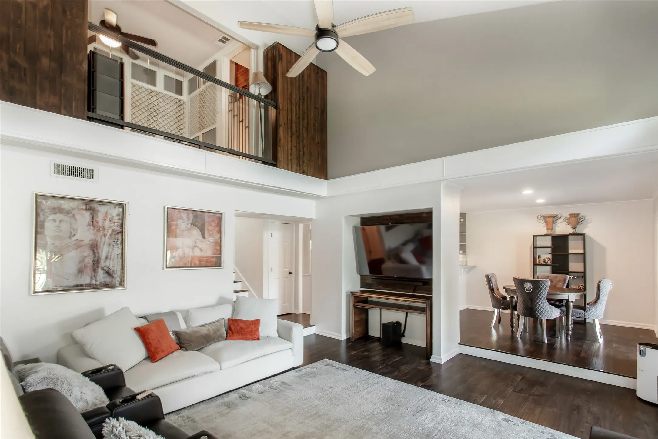 Vaulted ceiling with a ceiling fan, dark wood-finish flooring, and a second-story interior balcony with metal railings