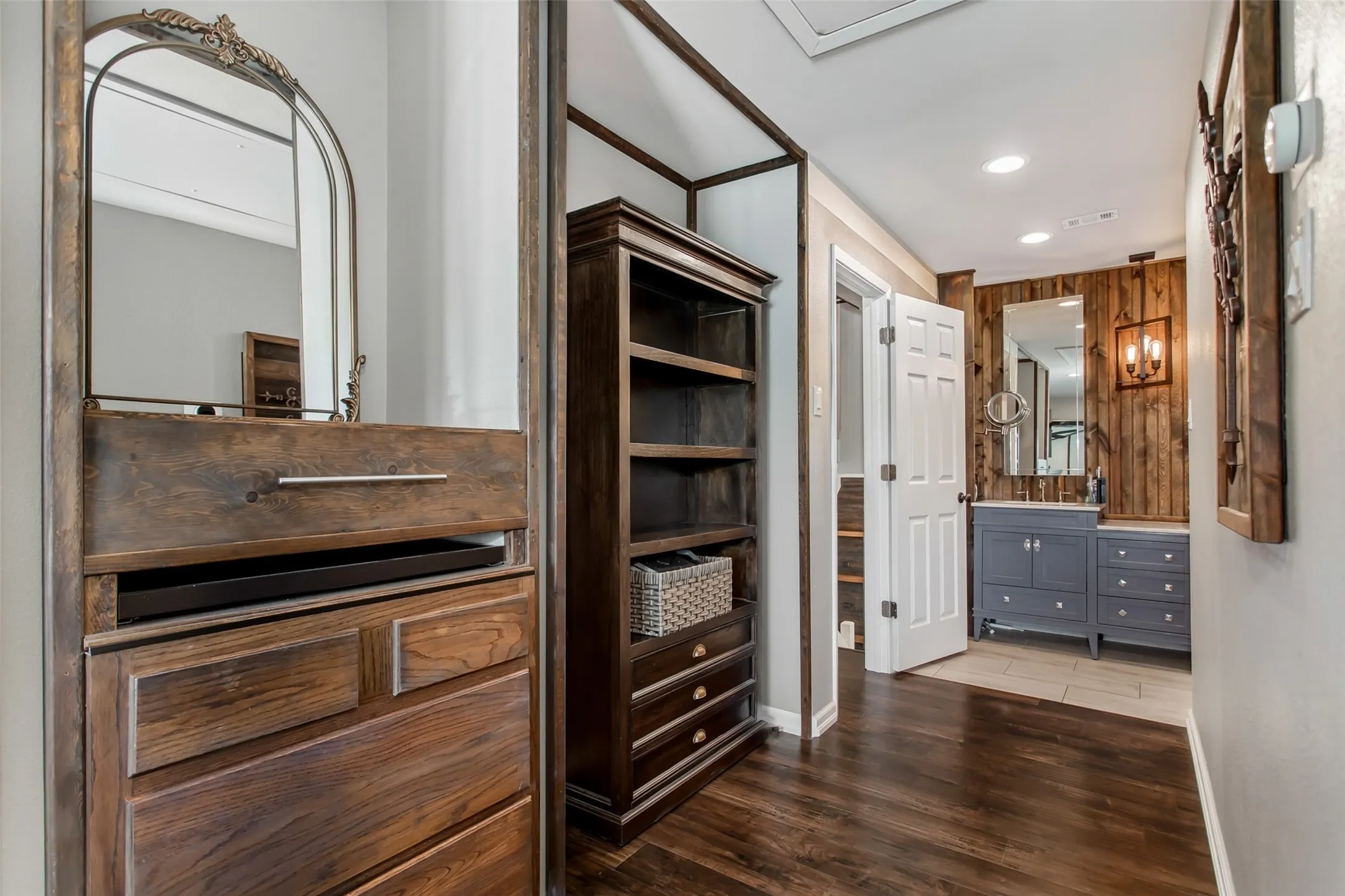 Dark wood-finish flooring with a modern vanity featuring dual sinks, a wood-paneled accent wall, and recessed ceiling lighting