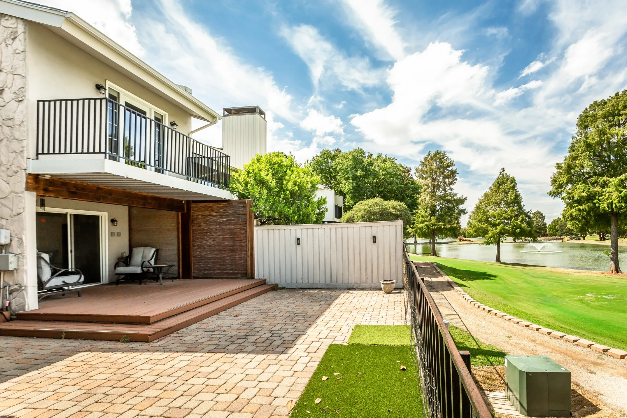 Two-story exterior with a ground-level patio featuring paver stones, a raised wood-finish deck, and a second-story balcony with dark railings