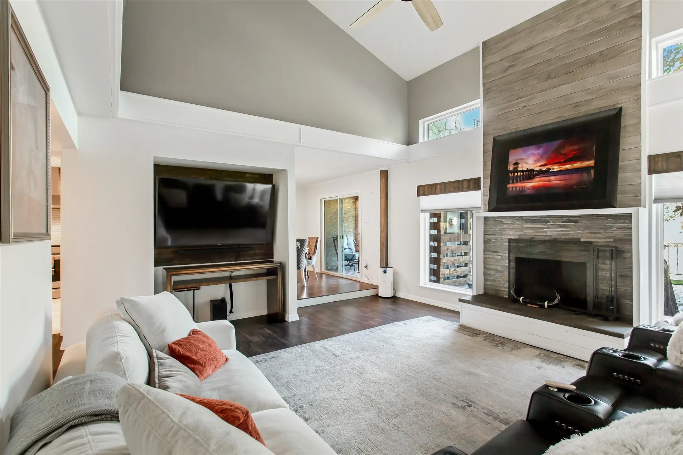 Vaulted ceiling with exposed beams, wood-finish flooring, stone-clad fireplace, and sliding glass doors