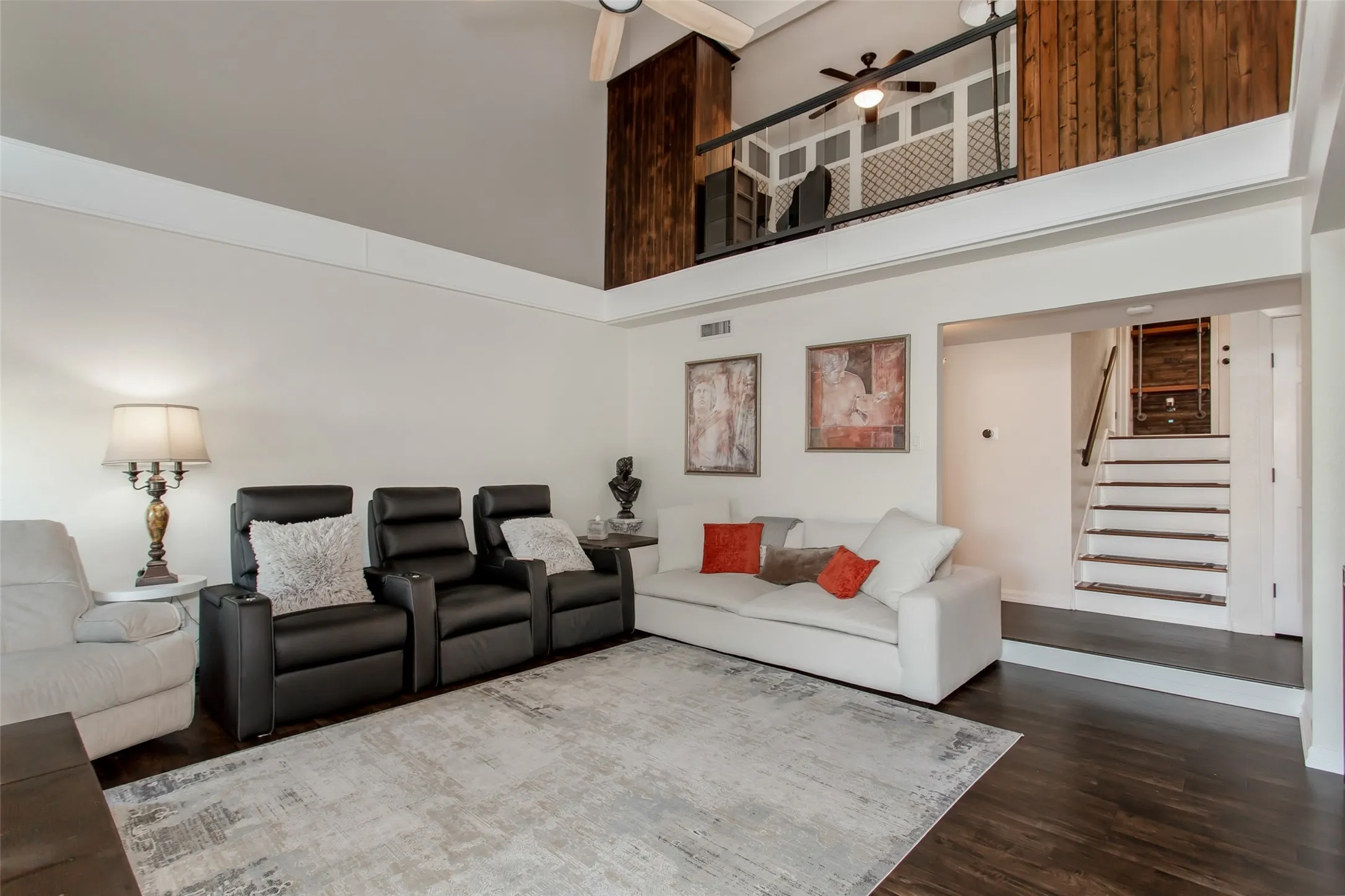 Spacious living area featuring high vaulted ceilings, rich wood-finish flooring, and a distinctive mezzanine with a decorative railing