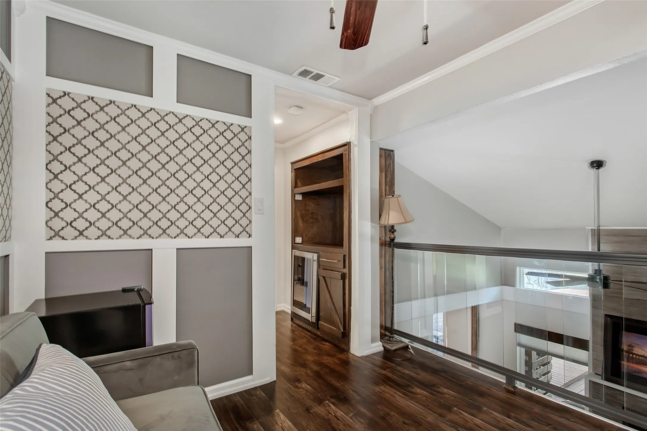 Wood-finish flooring, built-in cabinetry, glass railing, patterned accent wall, and ceiling fan
