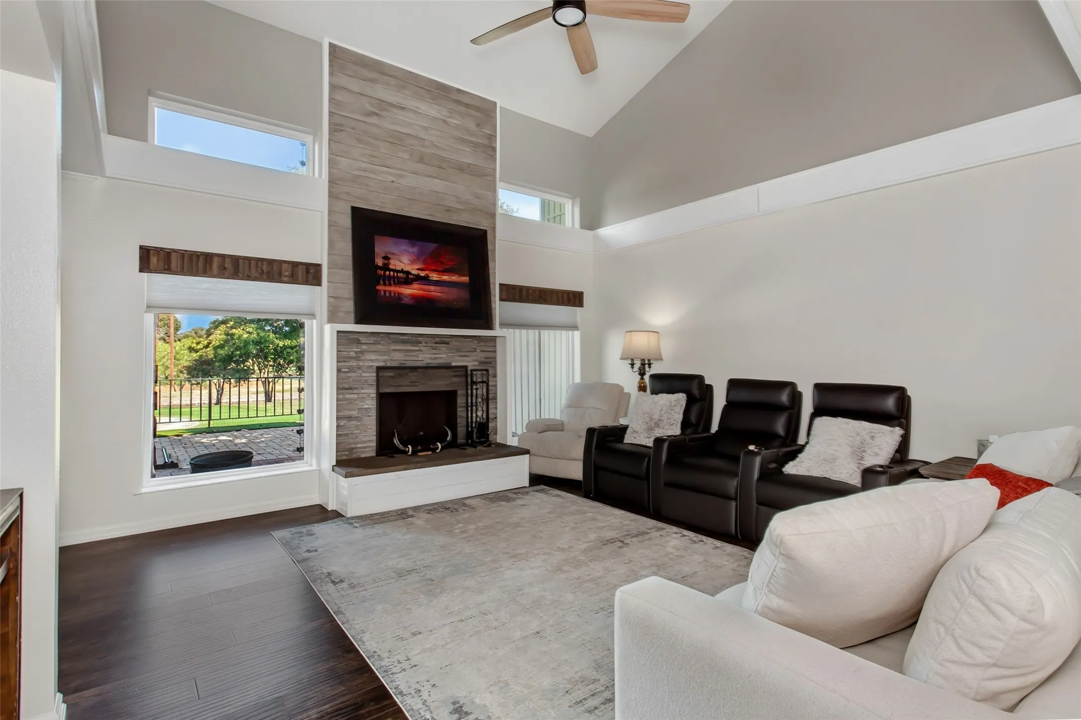 Living area featuring a vaulted ceiling with a ceiling fan, a fireplace with a stone surround and wood-finish accent wall, and wood-finish flooring