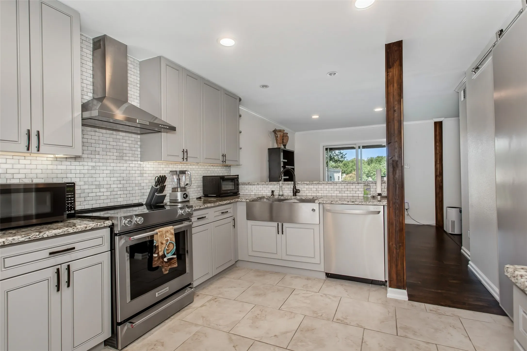Contemporary kitchen featuring light gray cabinetry, stainless steel appliances, white subway tile backsplash, granite countertops, and tile flooring