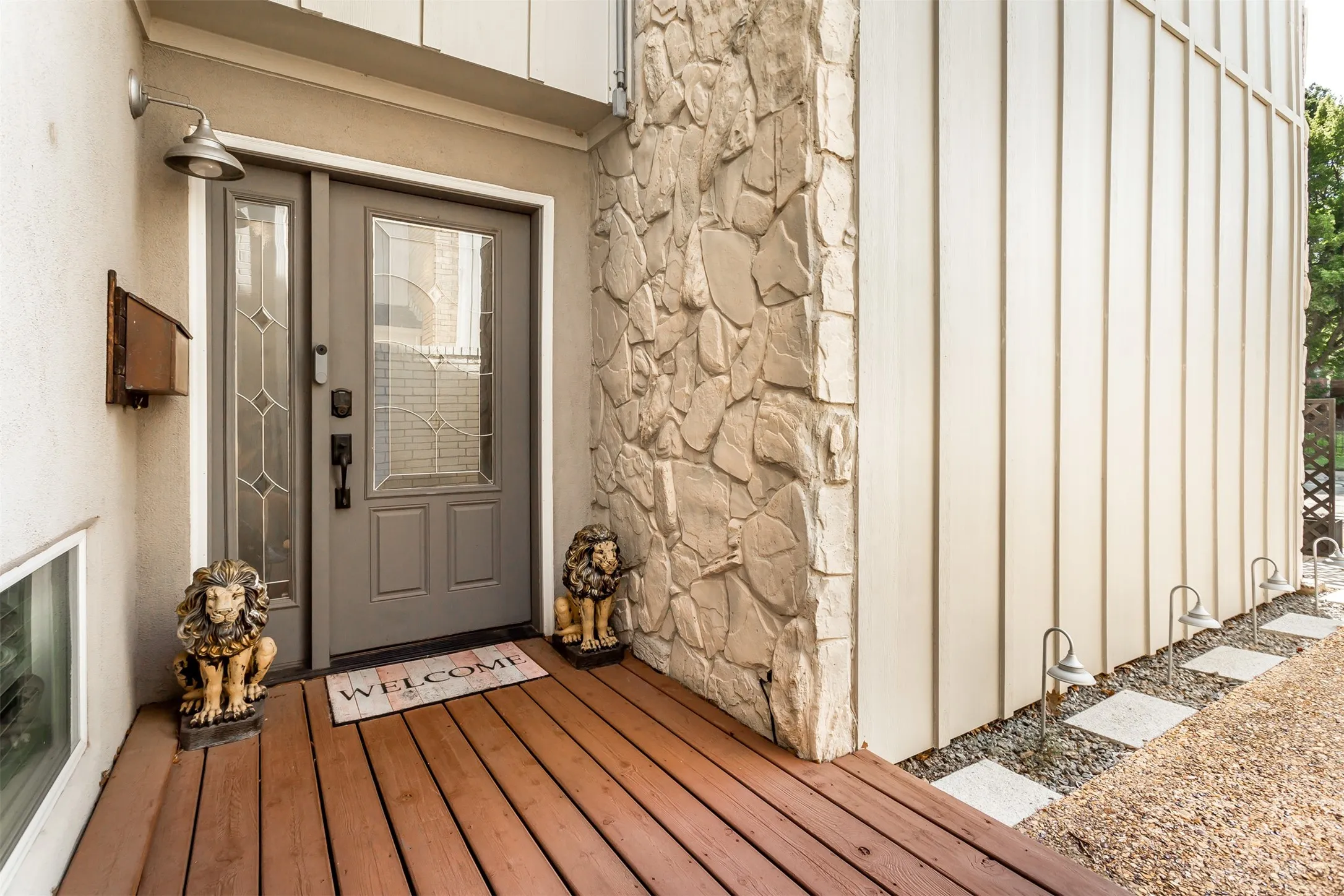 Entryway featuring a wood-finish porch, stone veneer siding, a gray door with decorative glass, and a wall-mounted light fixture