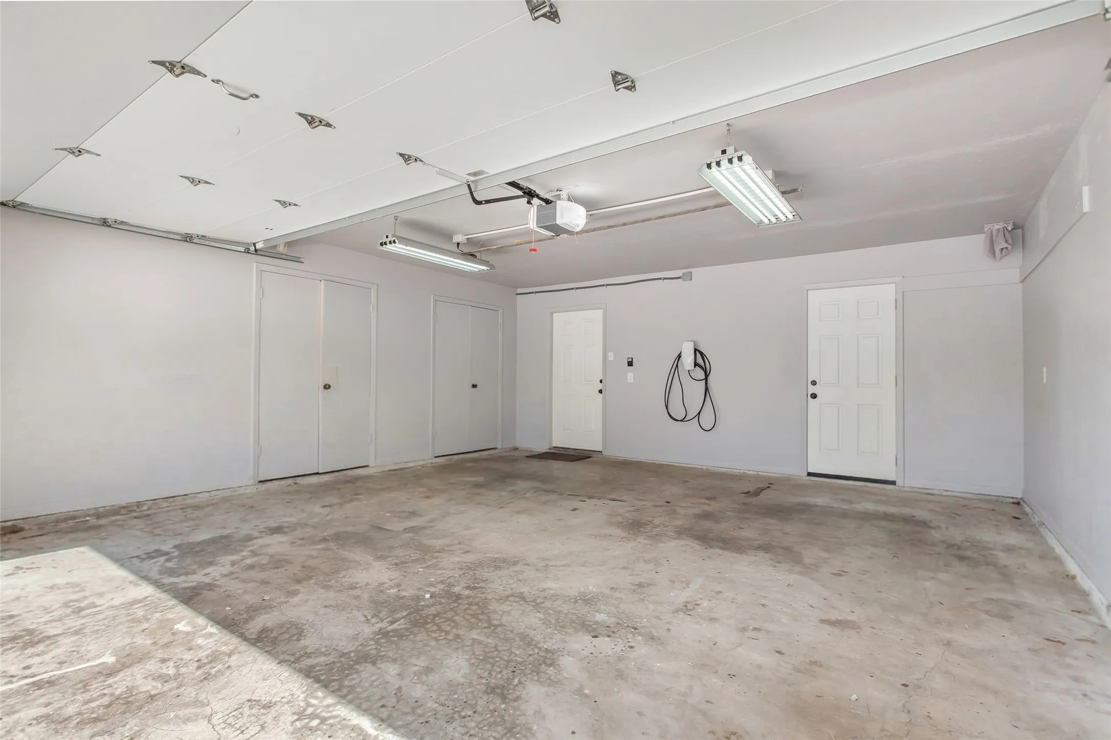 Spacious garage featuring epoxy-coated concrete flooring, recessed lighting throughout the ceiling, white panel garage doors, and mounted storage hooks for convenient organization
