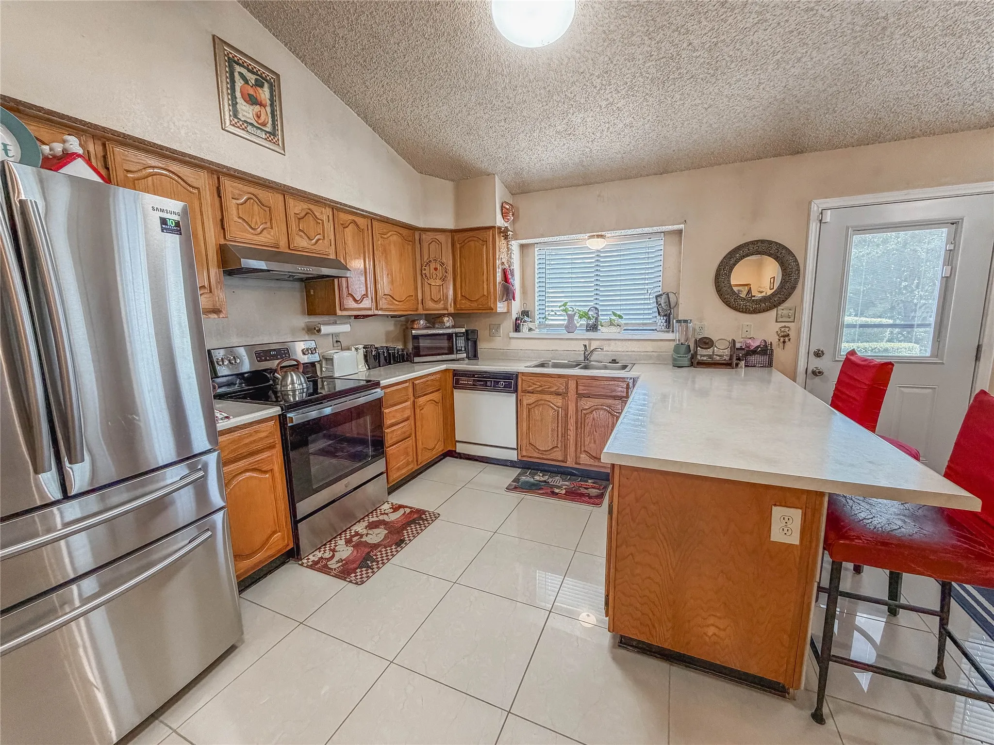 Kitchen featuring stainless steel appliances, wood cabinetry, light-toned countertops, and tile flooring