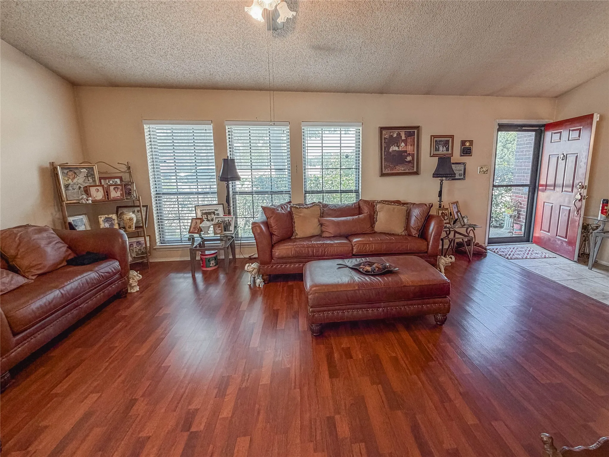 Wood-finish flooring throughout, multiple windows with blinds, and a red paneled entry door with a screen