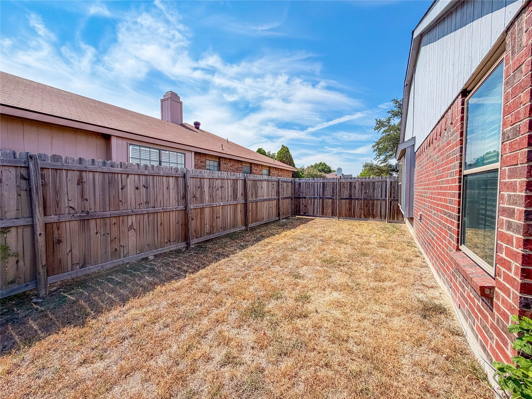 Fenced outdoor space with brick exterior, windows, and wood fencing
