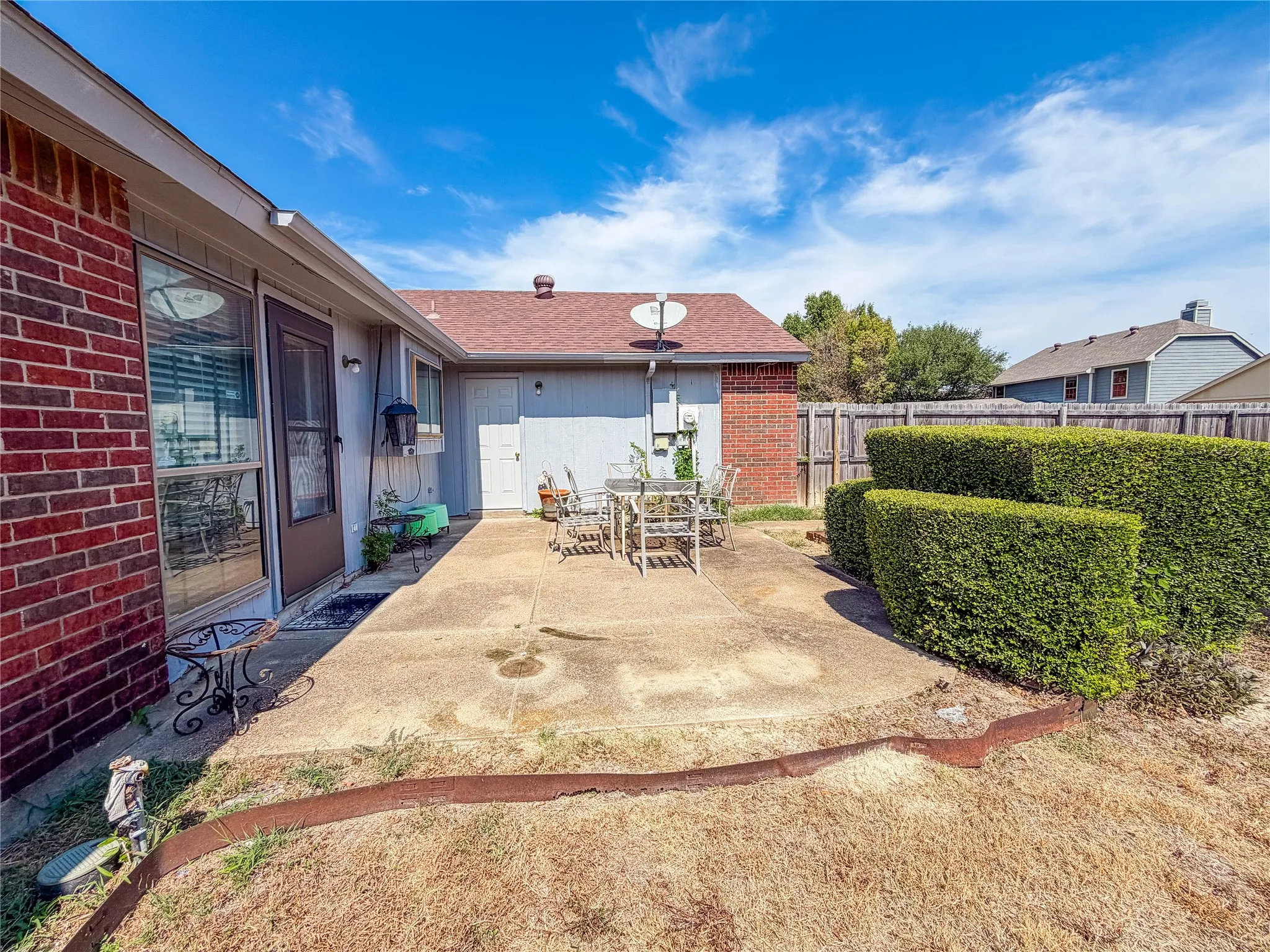 Red brick exterior, concrete patio, privacy fencing, manicured hedges, and exterior entry door
