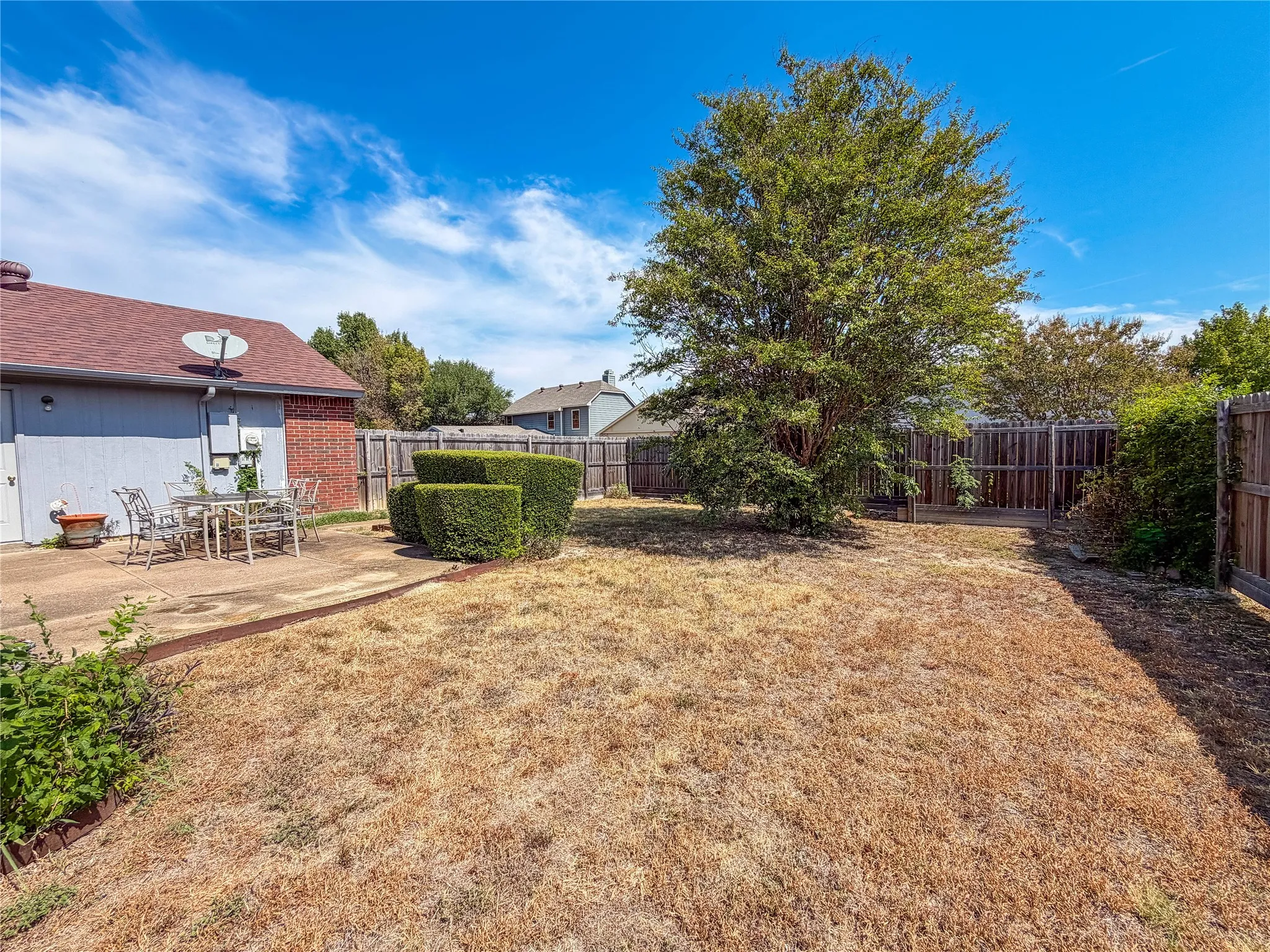 Paved patio with direct access to the structure, complemented by manicured shrubbery and a mature tree, all enclosed by a wood privacy fence