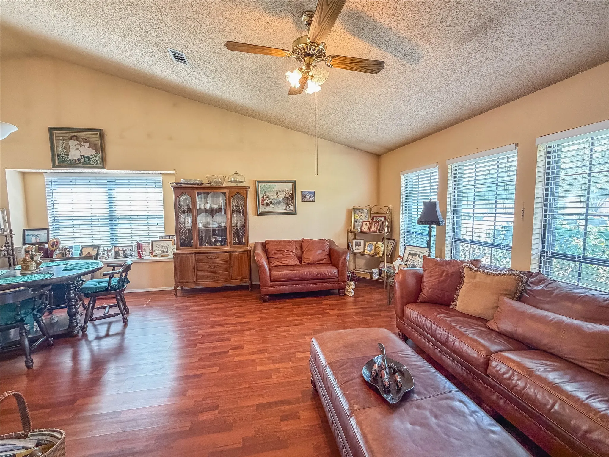 Vaulted ceiling with a ceiling fan, wood-finish flooring, and multiple windows with blinds