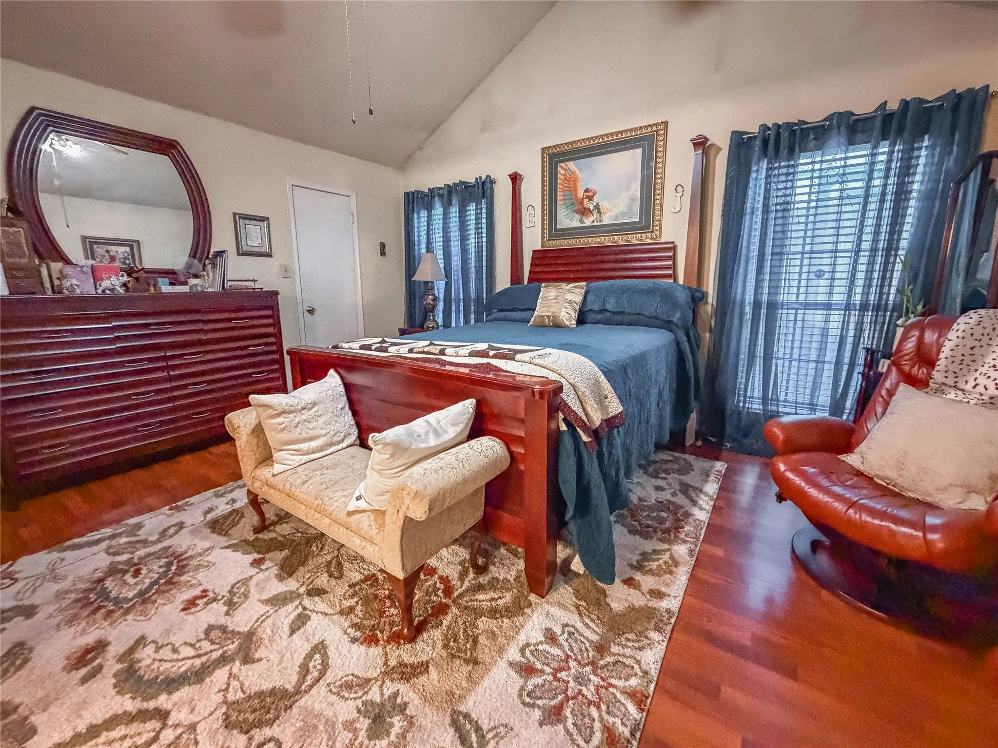Vaulted ceiling, polished wood-finish flooring, and window with blinds