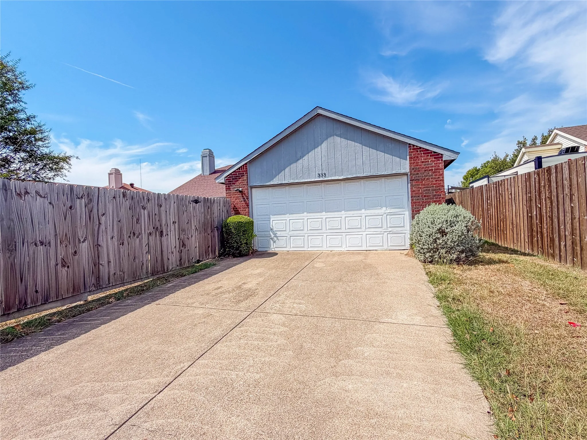 Brick exterior with a two-car garage, concrete driveway, and wood privacy fencing