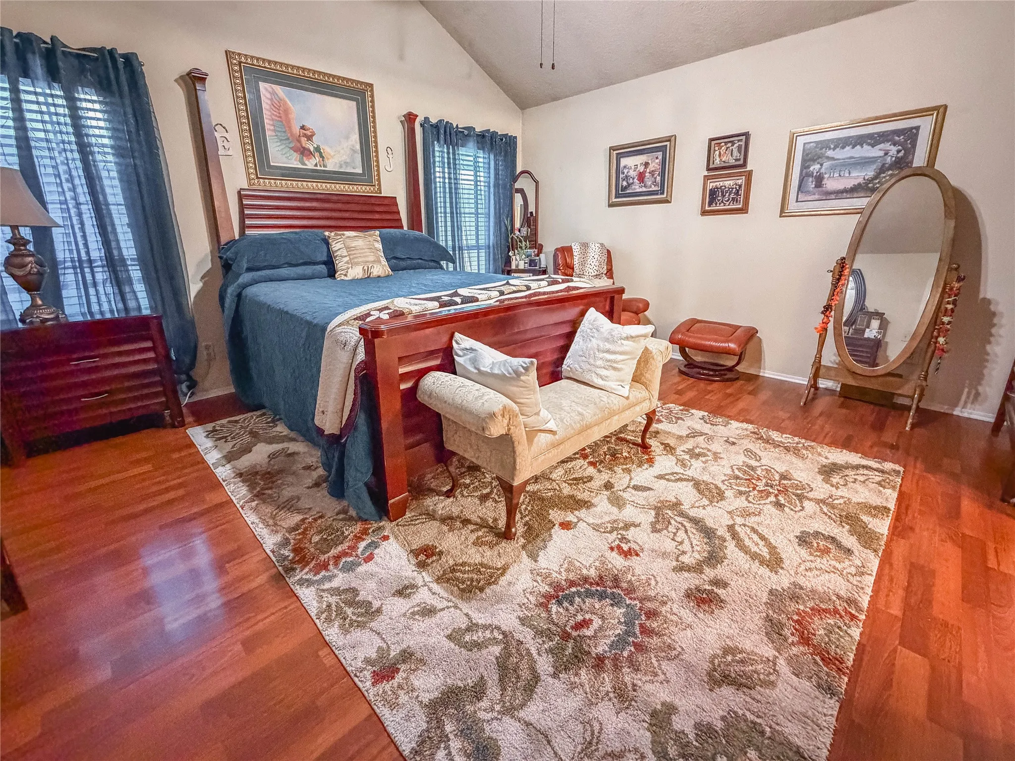 Vaulted ceiling with a ceiling fan, rich wood-finish flooring, and window treatments