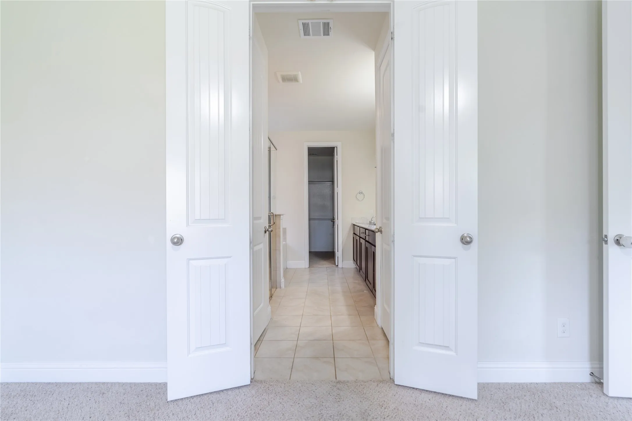 Double entry doors opening to a space with tile flooring, a dark wood-finish vanity, and light-colored walls