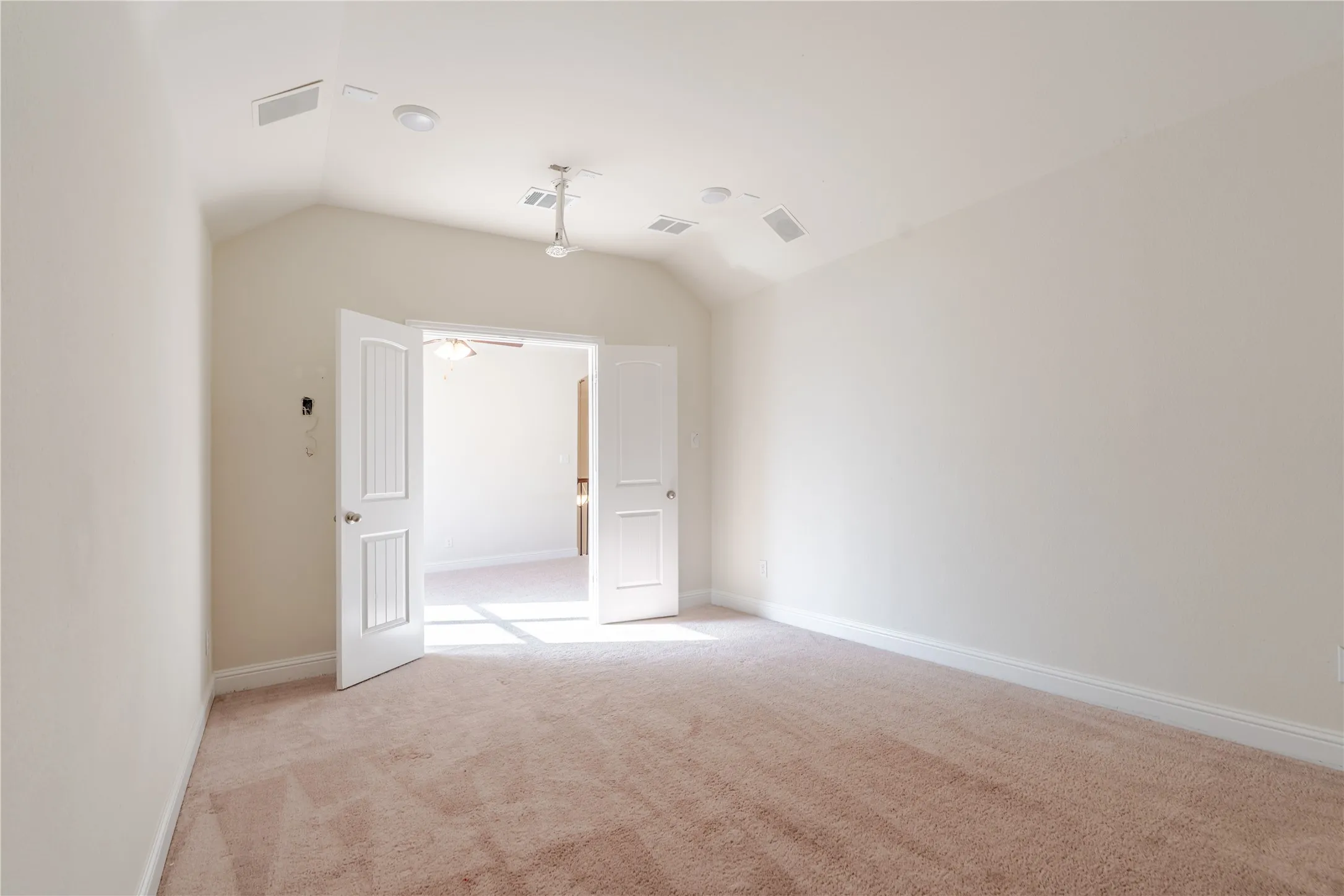 Spacious room featuring vaulted ceilings, plush carpeting, white baseboards, and double paneled doors