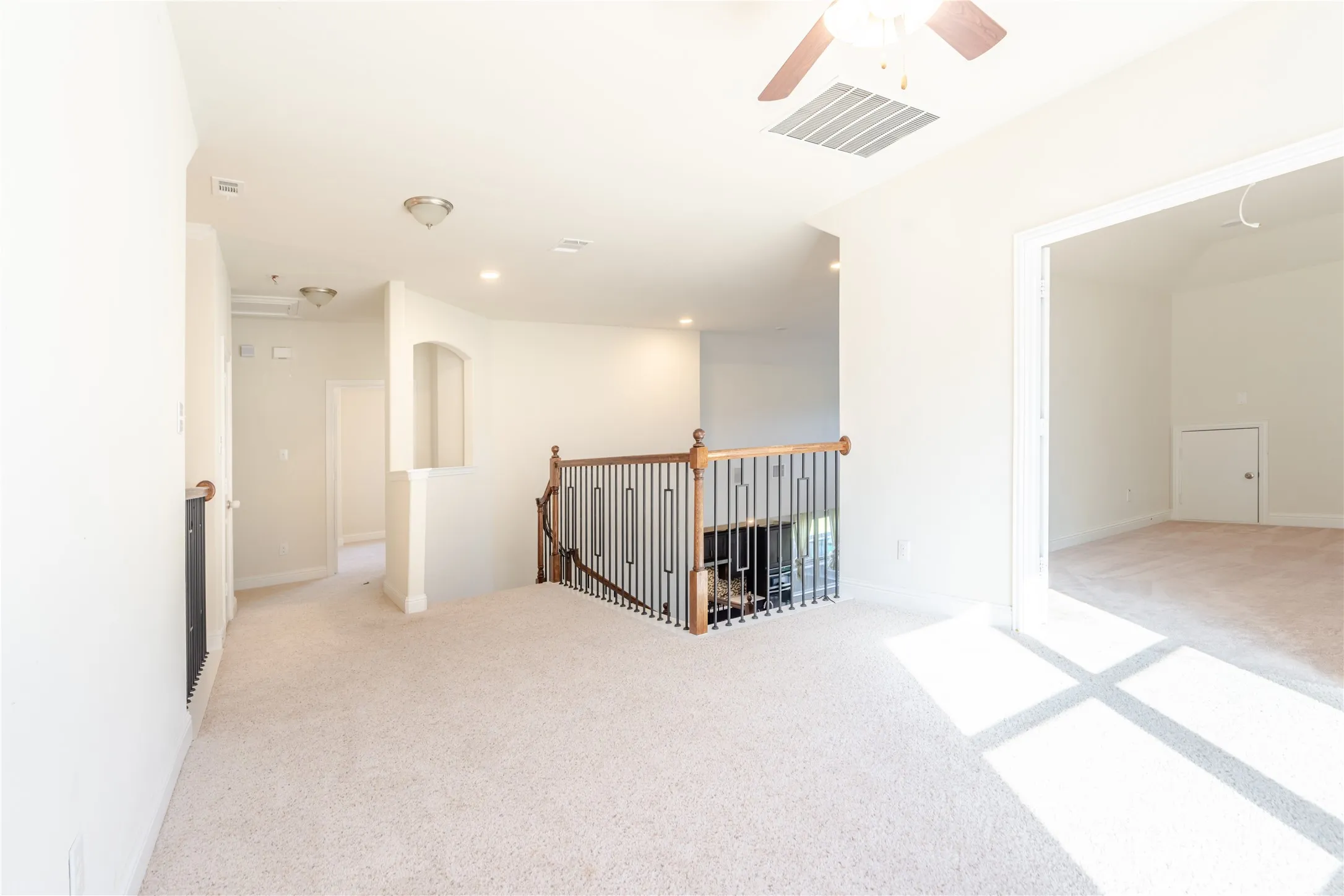 Upper-level hallway featuring carpet flooring, a ceiling fan with light fixture, recessed lighting, a staircase with wood handrail and wrought iron balusters, and an arched entryway to an additional room