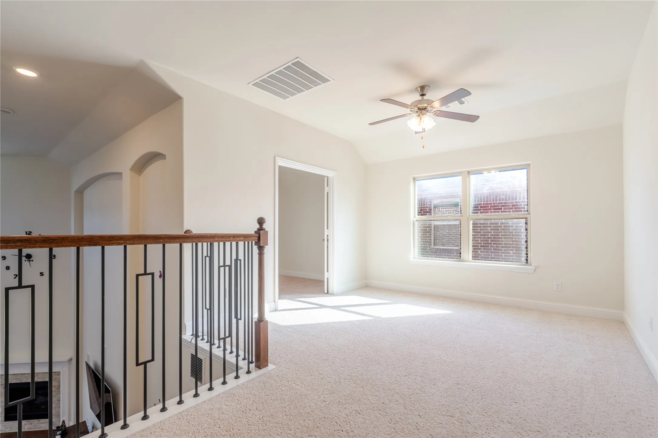 Carpeted loft area featuring a ceiling fan, a large window, and arched doorways
