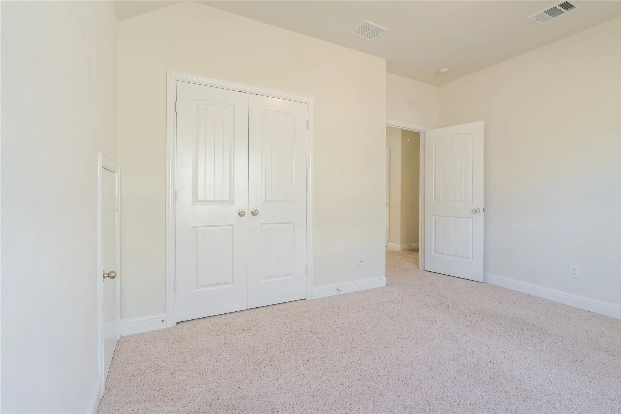Neutral-toned room featuring a light-colored carpet, white baseboards, and a pair of white paneled bifold doors