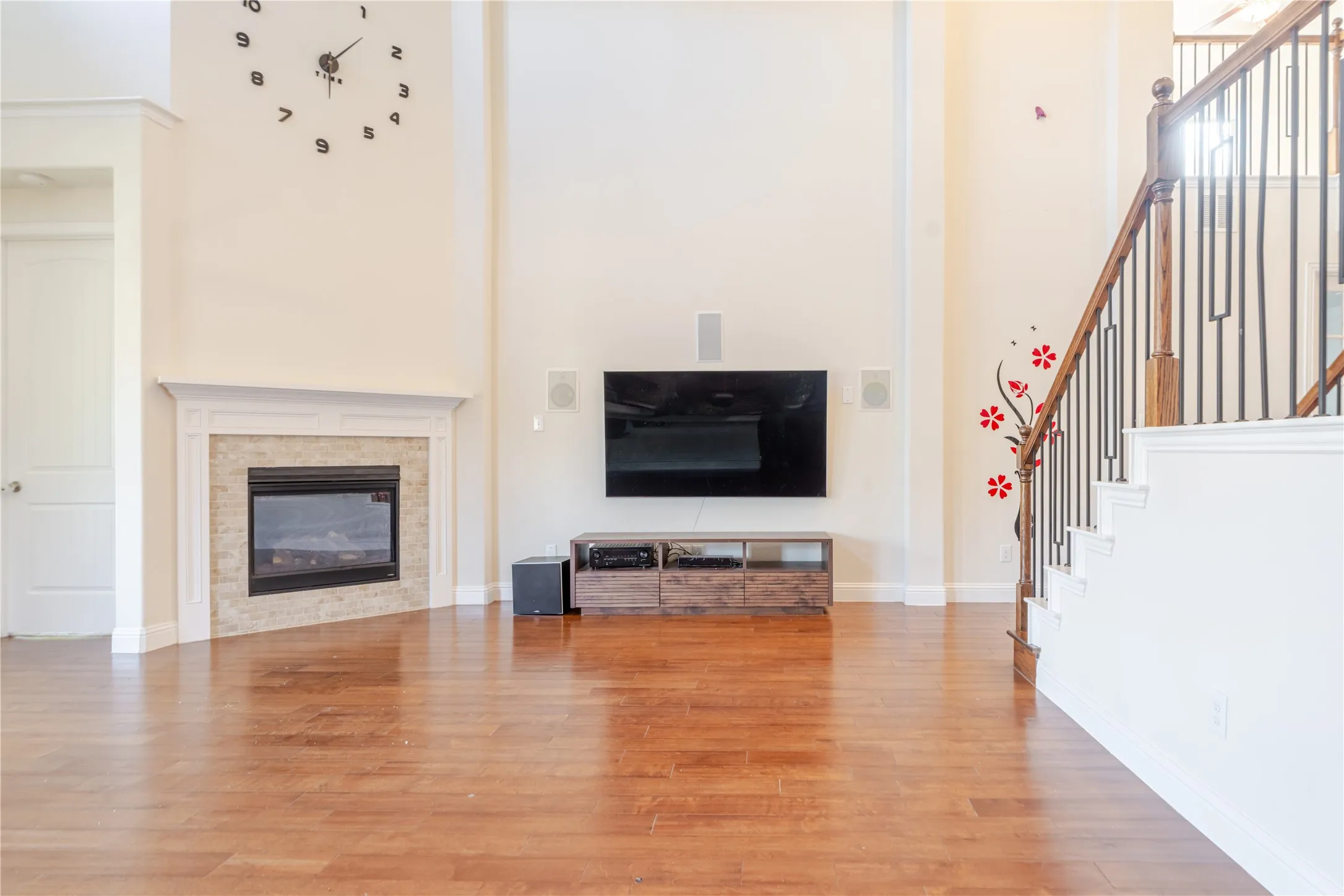 Spacious living area featuring high ceilings, wood-finish flooring, a corner fireplace with a stone surround, and an open staircase with wood handrails and black iron balusters