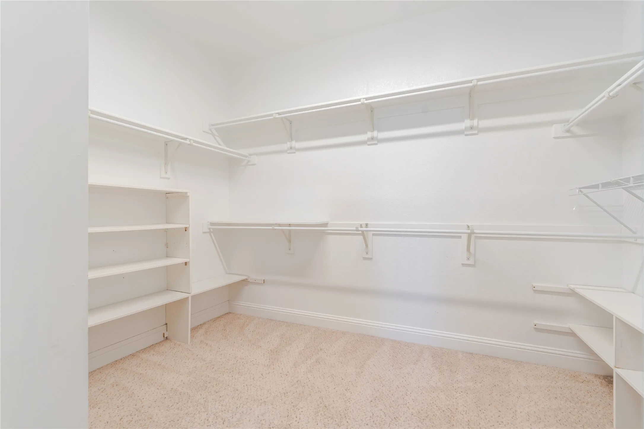 Expansive walk-in closet featuring white wall-mounted shelving and hanging rods