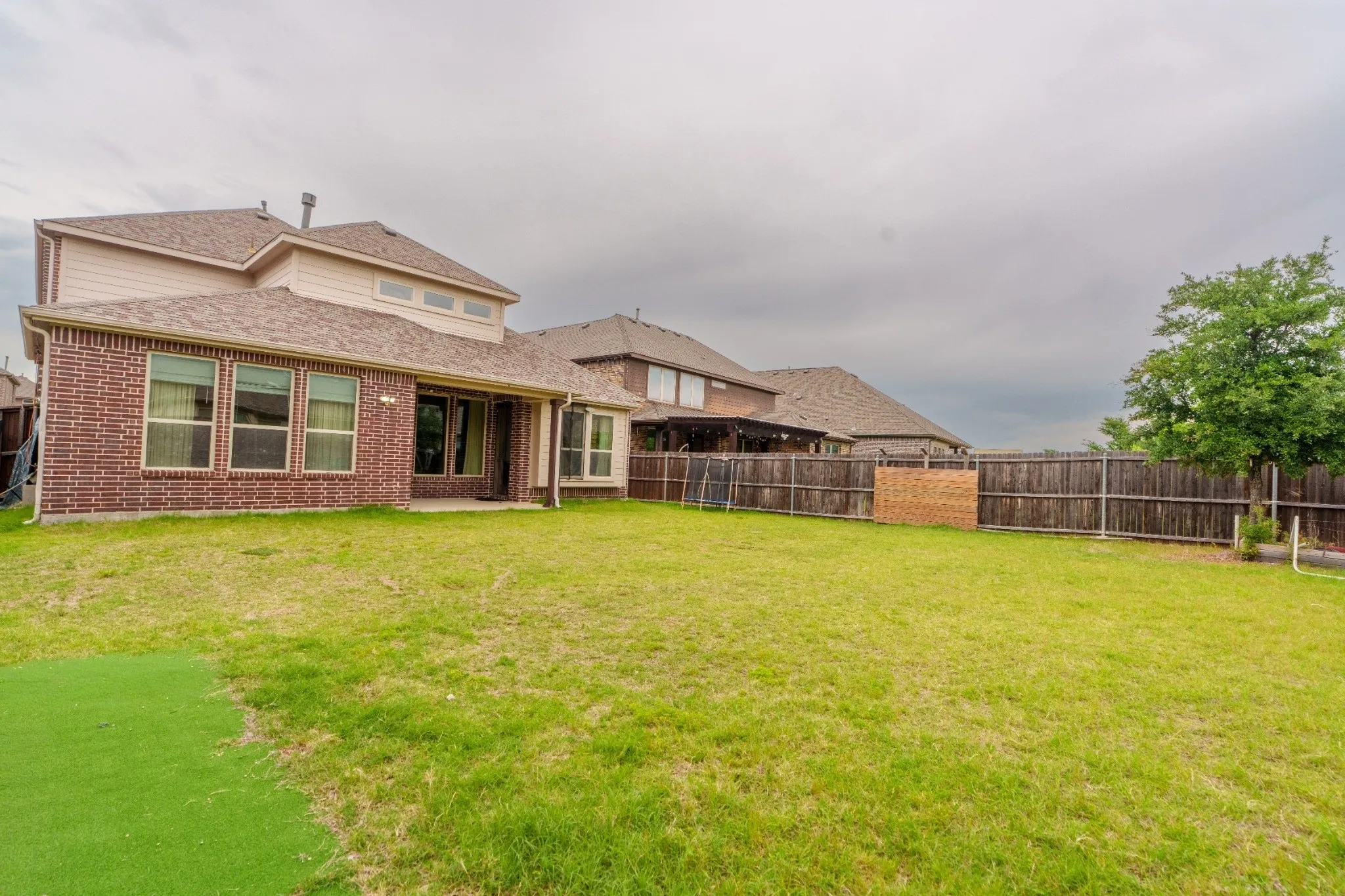 Spacious backyard featuring a large grass area, a partial artificial turf section, and a wood privacy fence