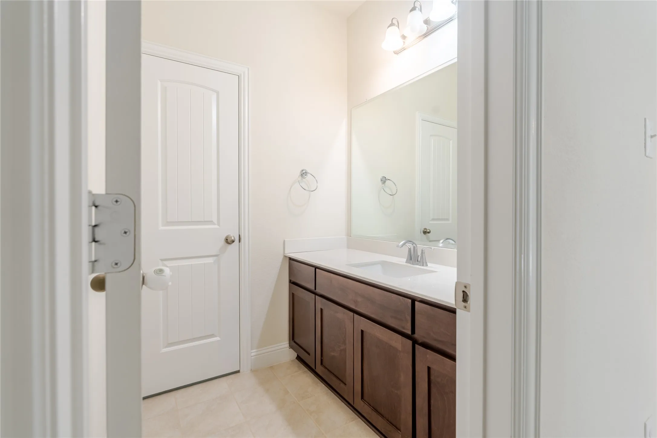Bathroom vanity featuring a single sink set into a light-colored countertop, dark wood-finish cabinetry, and a large wall-mounted mirror