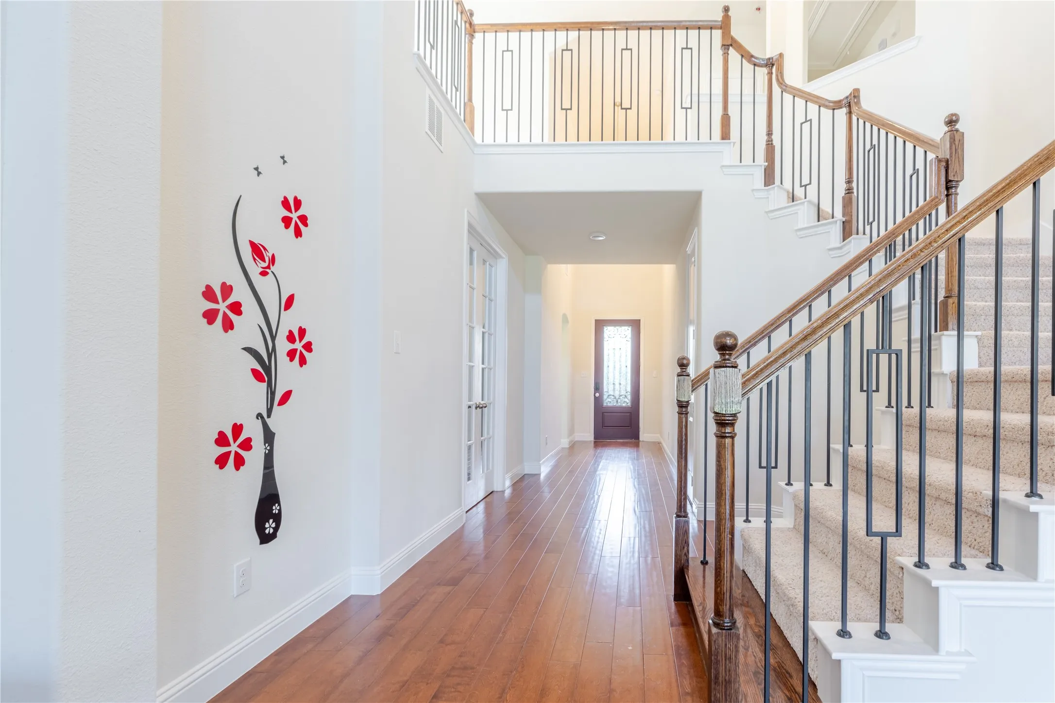 Two-story entryway featuring wood-finish flooring, a carpeted staircase with wood handrails and wrought iron balusters, and a second-floor landing with matching railings