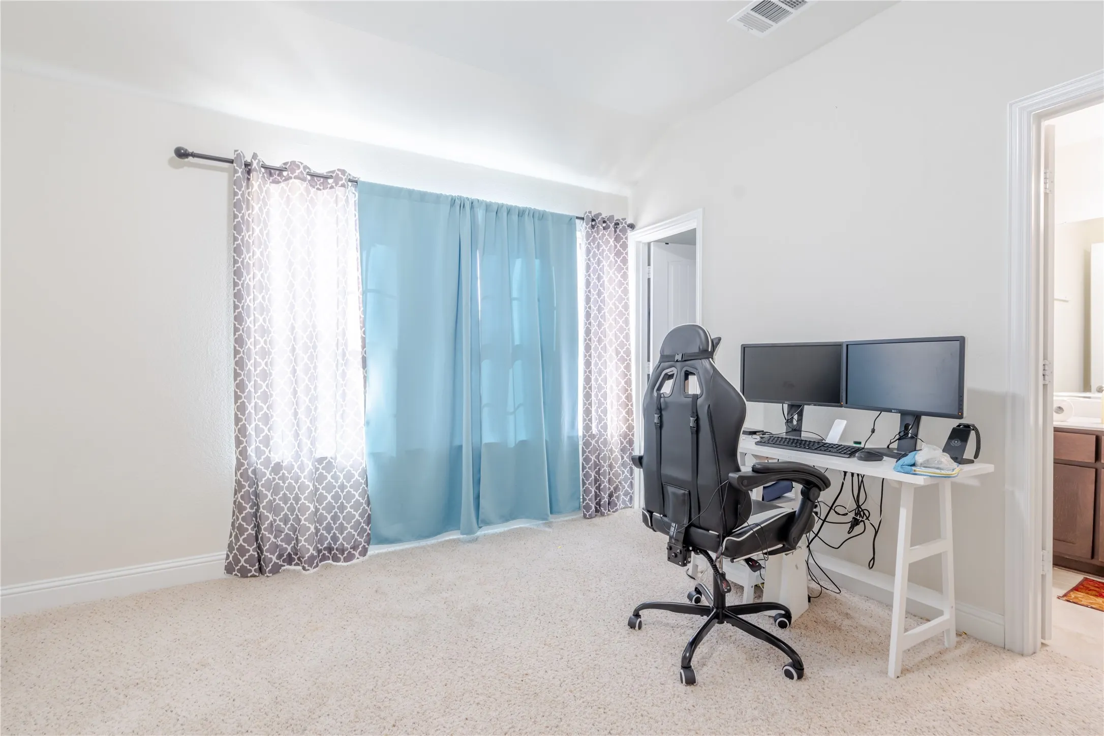 Carpeted room with a window featuring a curtain rod, light blue sheer drapes, and patterned gray and white curtains