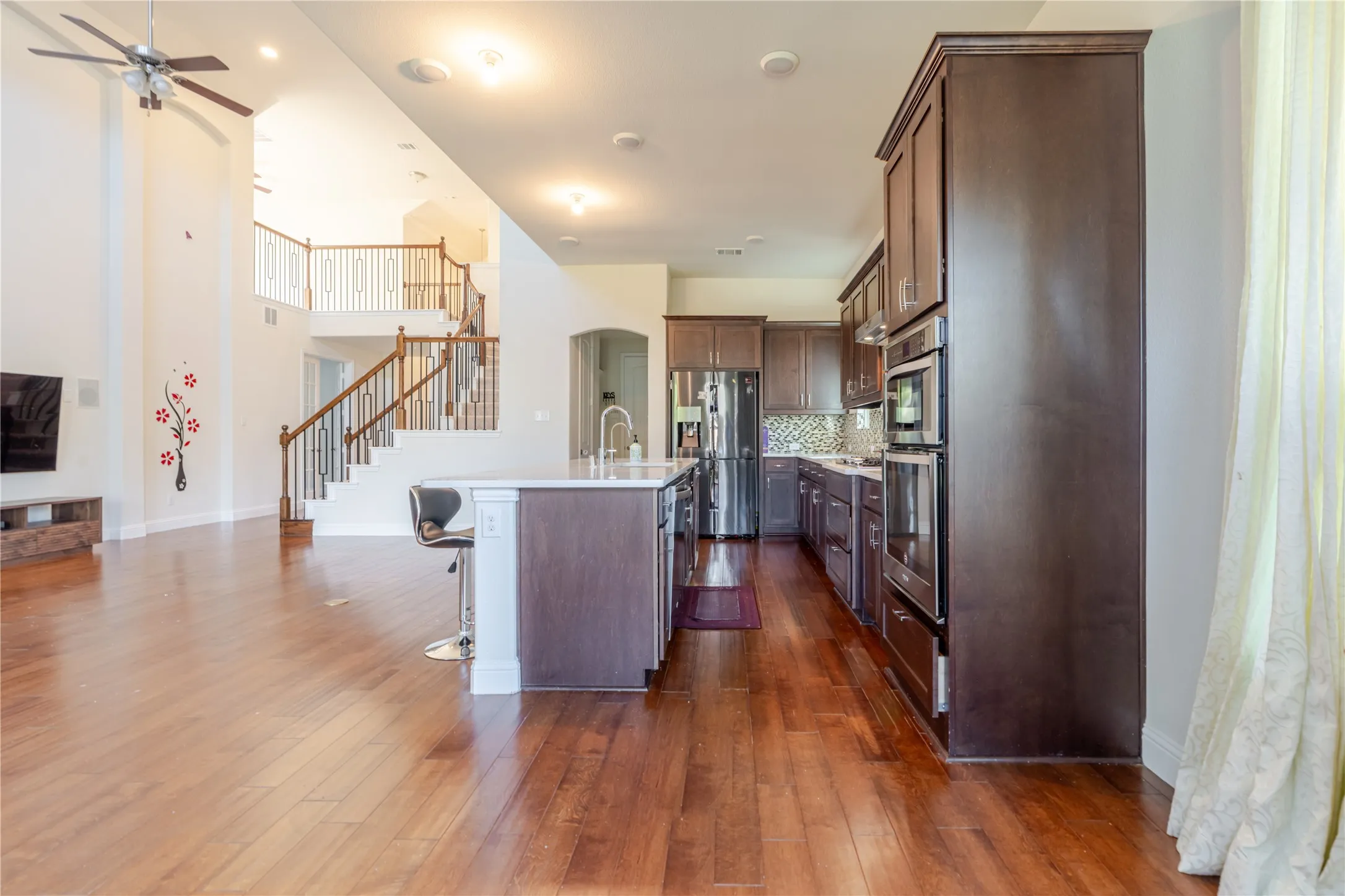 Open-concept living space with wood-finish flooring, a two-story ceiling, and a prominent staircase featuring wood handrails and wrought iron balusters