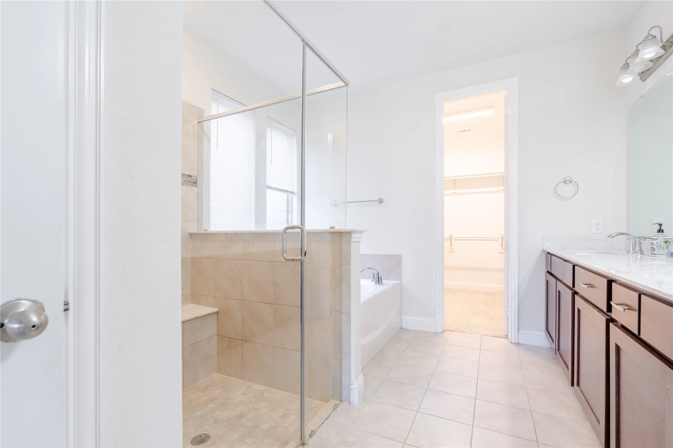 Bathroom featuring a glass-enclosed shower with tiled bench, separate soaking tub, dual vanity with stone countertop, and tile flooring