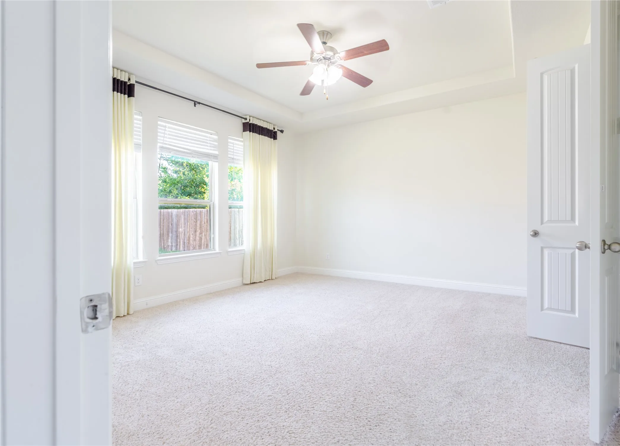 Spacious room featuring light-colored carpeting, a tray ceiling, and a ceiling fan with integrated lighting
