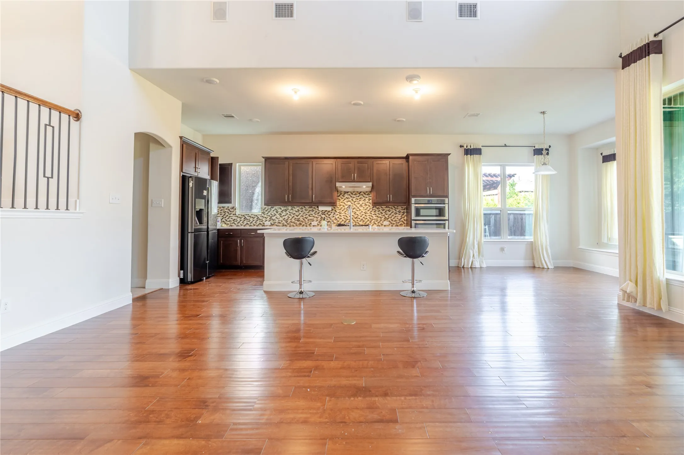 Spacious open-concept living area featuring gleaming wood-finish flooring, a kitchen island with seating, dark wood cabinetry, and a mosaic tile backsplash
