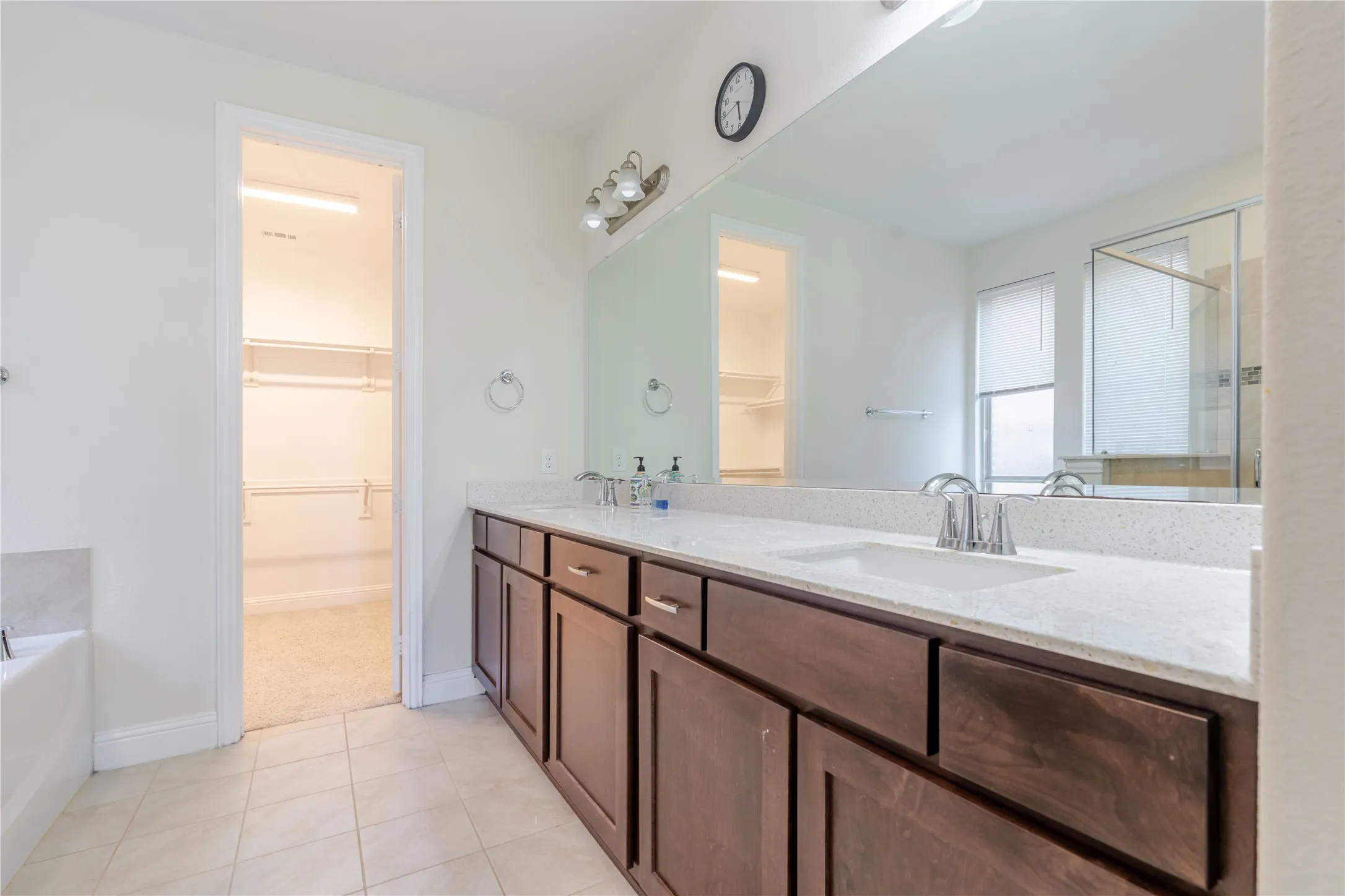 Bathroom featuring a double vanity with stone-finish countertops, dark wood cabinetry, and a large wall-mounted mirror