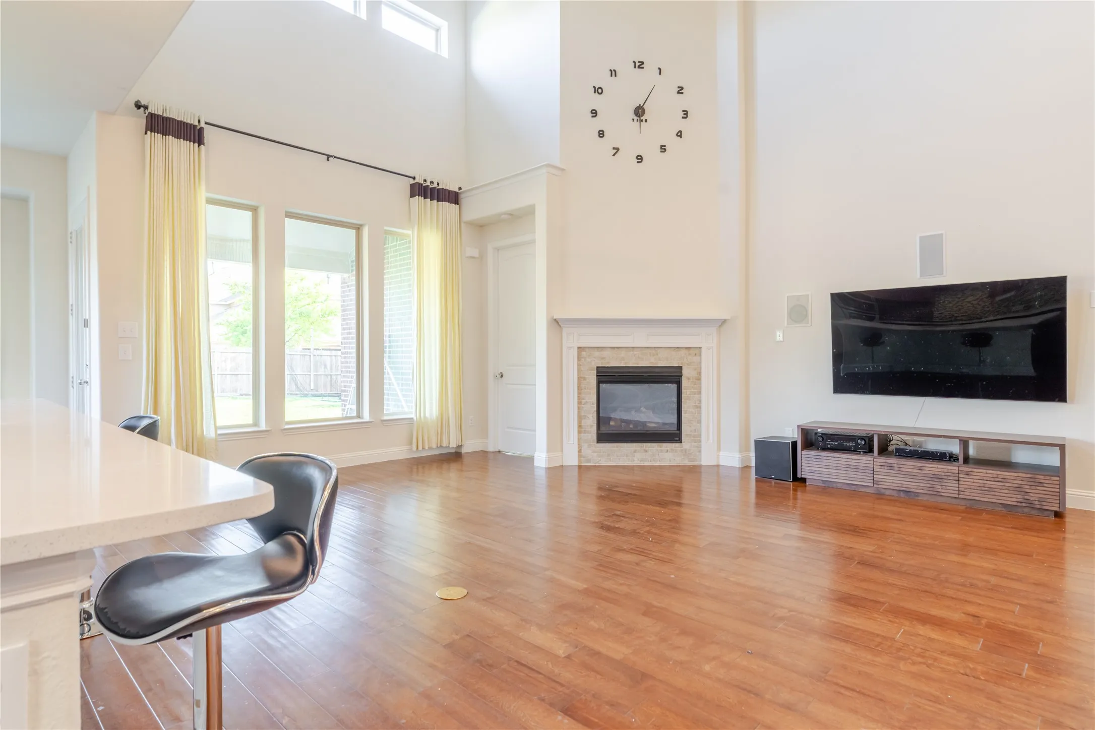 Spacious living area featuring high ceilings, wood-finish flooring, and a fireplace with a stone tile surround
