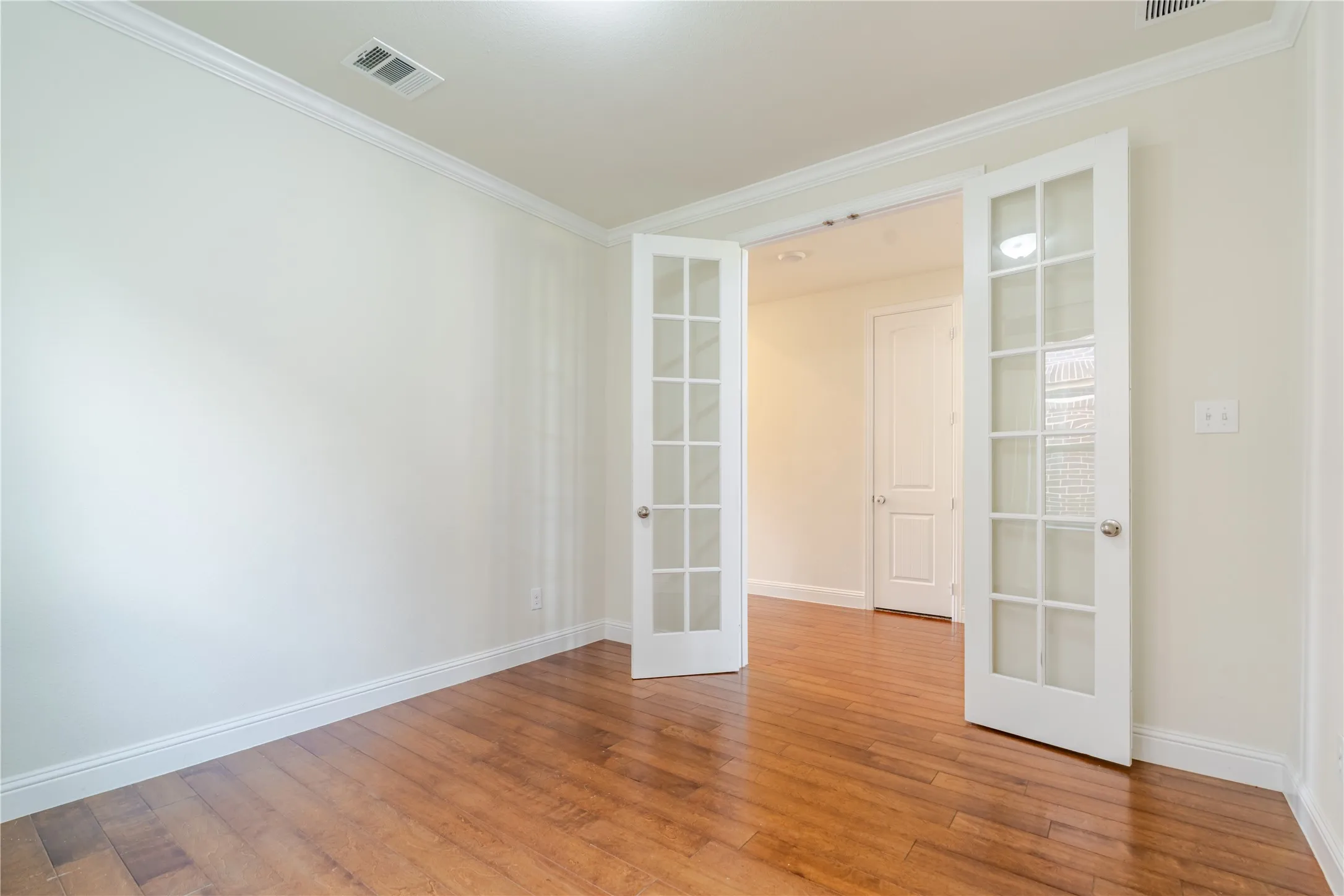 Room with wood-finish flooring, white walls, and crown molding